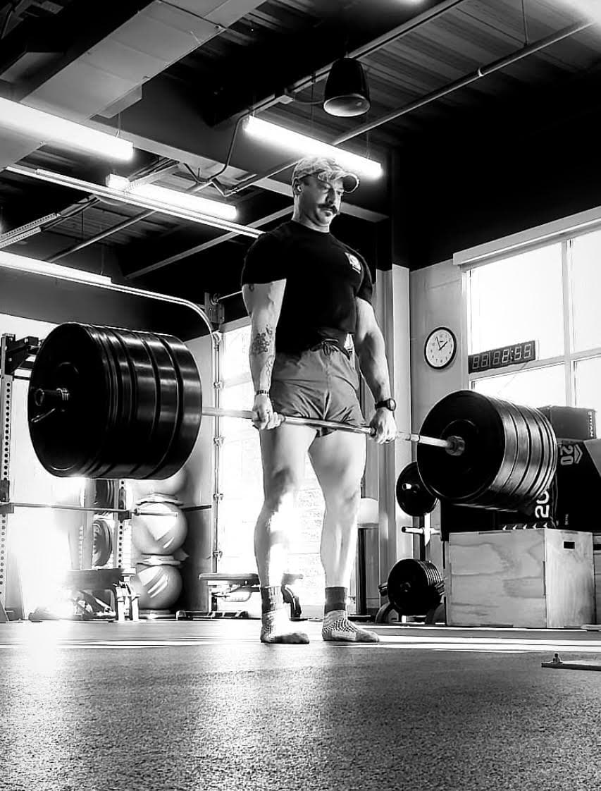 Brian deadlifting a heavily loaded barbell in a gym